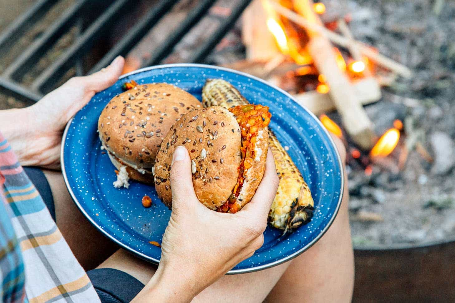 Megan holding a plate with two lentil sloppy joes near a campfire