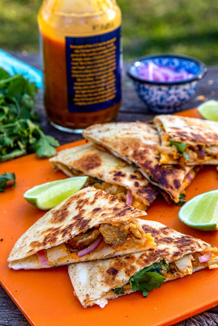 Sliced quesadillas stacked on an orange cutting board with slices of lime.