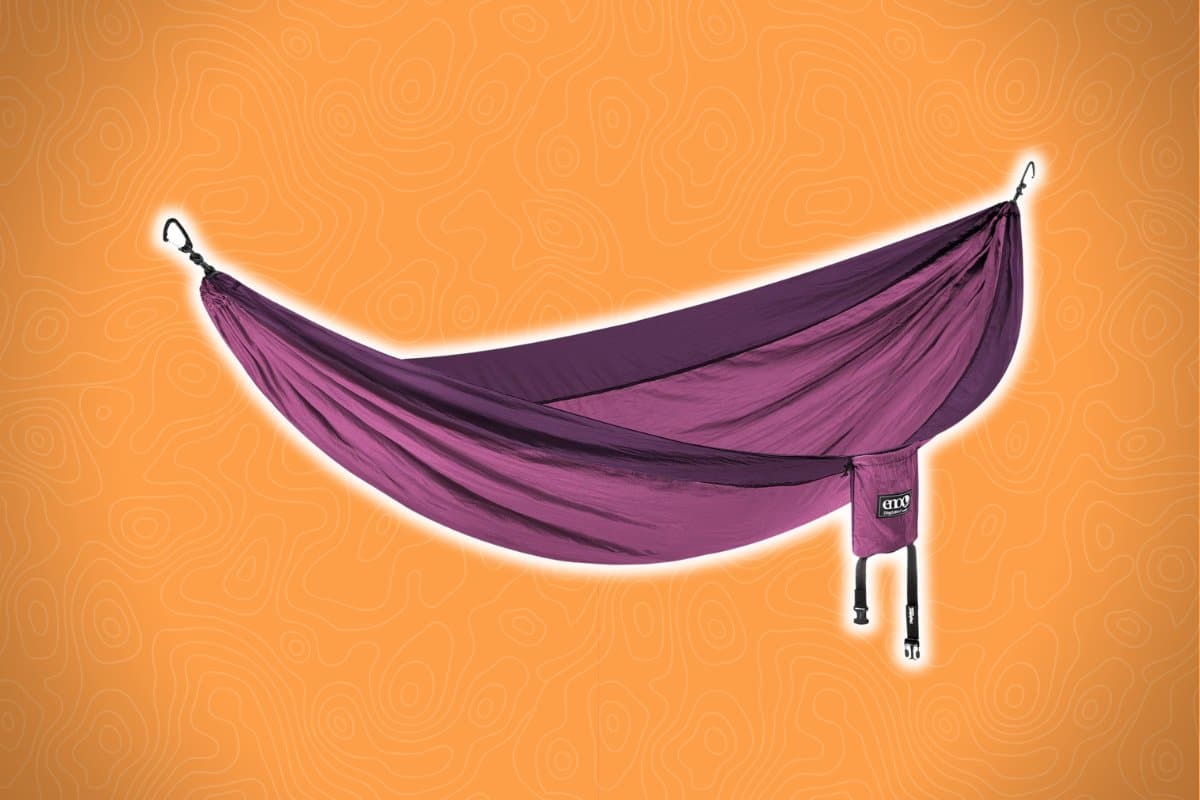 A purple hammock with black straps is suspended and fully extended against an orange background with a subtle abstract pattern.