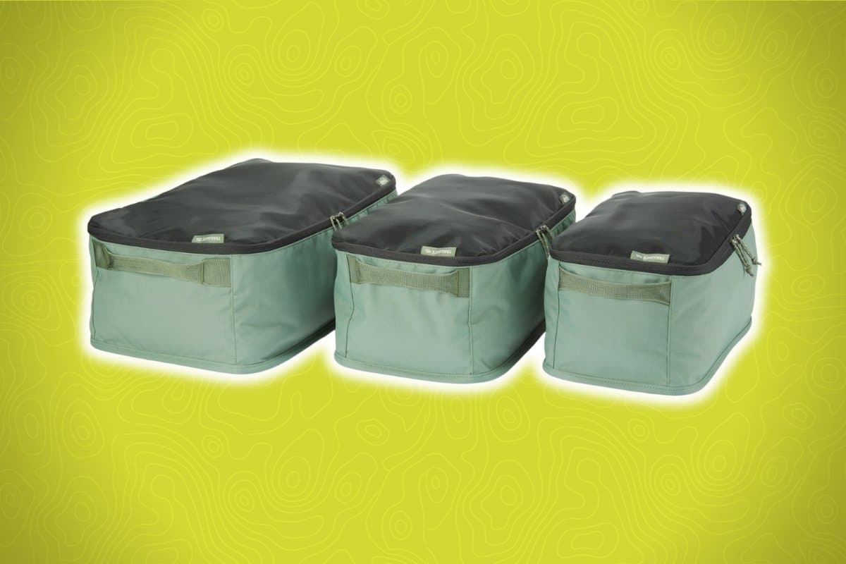 Three green and black packing cubes of varying sizes are placed on a bright yellow background with a subtle abstract pattern.