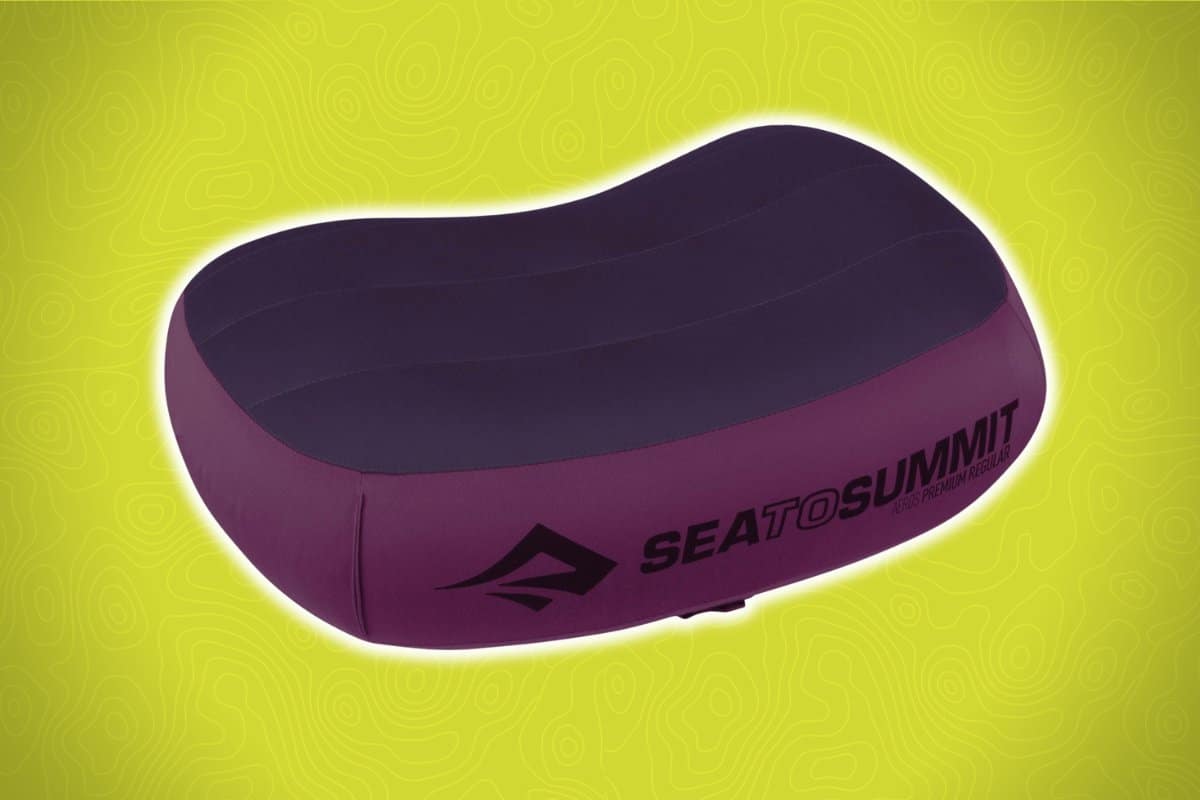 A dark purple inflatable travel pillow with the "Sea to Summit" logo on the side is set against a green background with subtle swirling patterns.