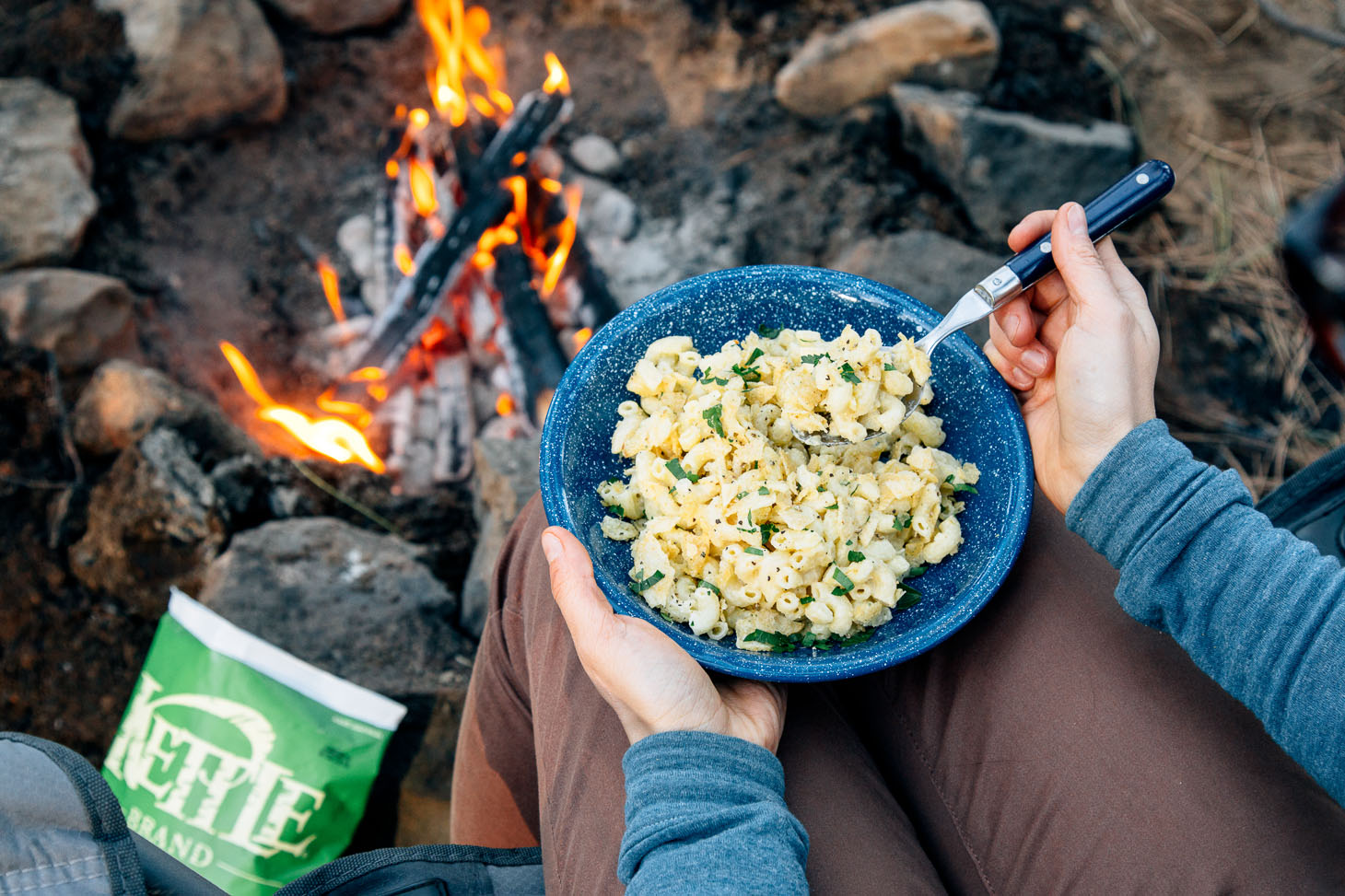 Mac and cheese in a blue camping bowl next to a fire.